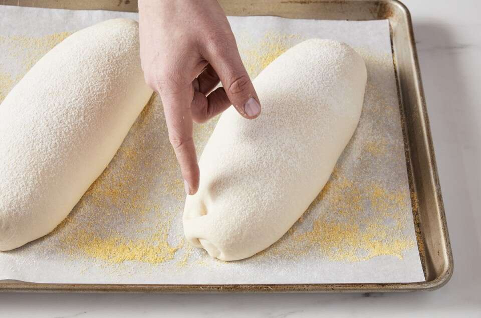 Baker pressing finger into proofed bread dough to gauge proofing