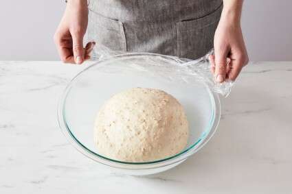 Baker uncovering a bowl of proofing bread dough